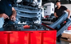 Mechanik carrying truck bumper, truck front in background