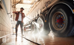 A truck wash employee disinfects a wheel of a trailer