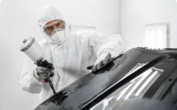 Varnisher spraying black paint over bodywork of car